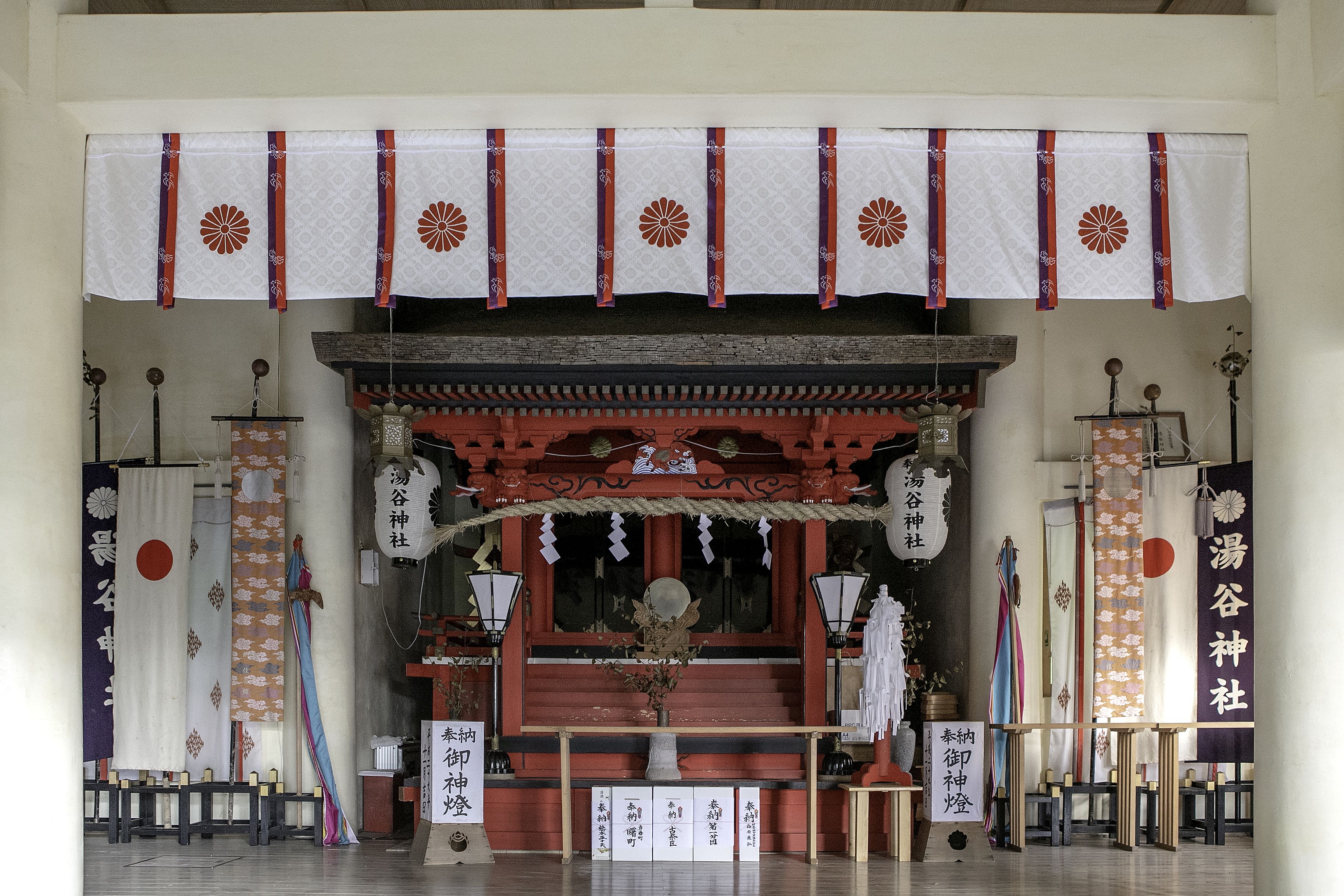 A traditional Japanese shrine with a red torii gate, white and orange banners, and a stone altar.