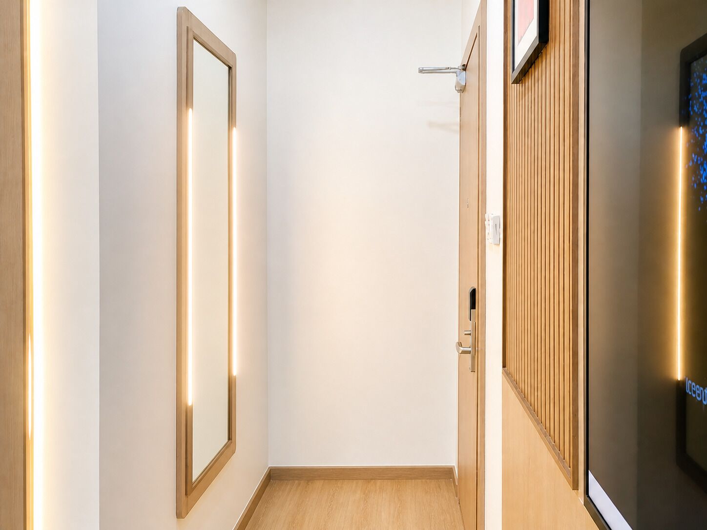 Un pasillo con piso de madera, una puerta con interruptor de luz y un aplique en la pared.