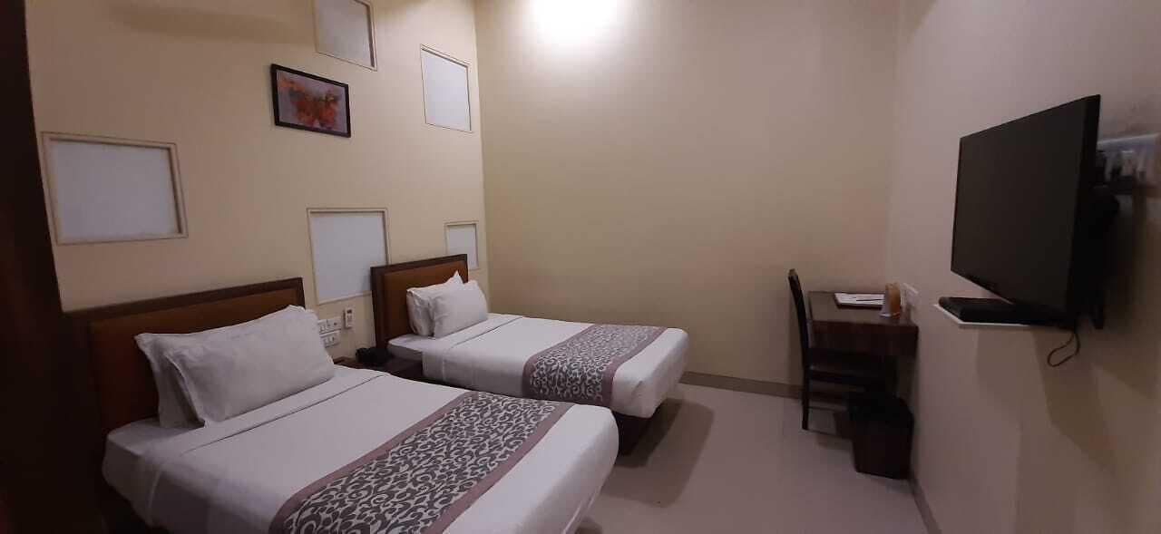 A hotel room with two beds, a TV, and a desk with a chair.