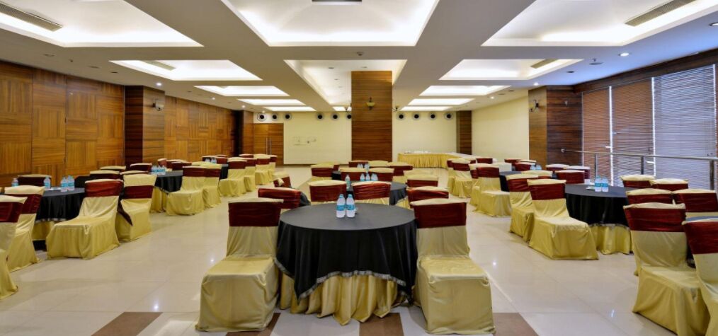 Un salón de conferencias con mesas y sillas redondas, paneles de madera y un amplio ventanal.
