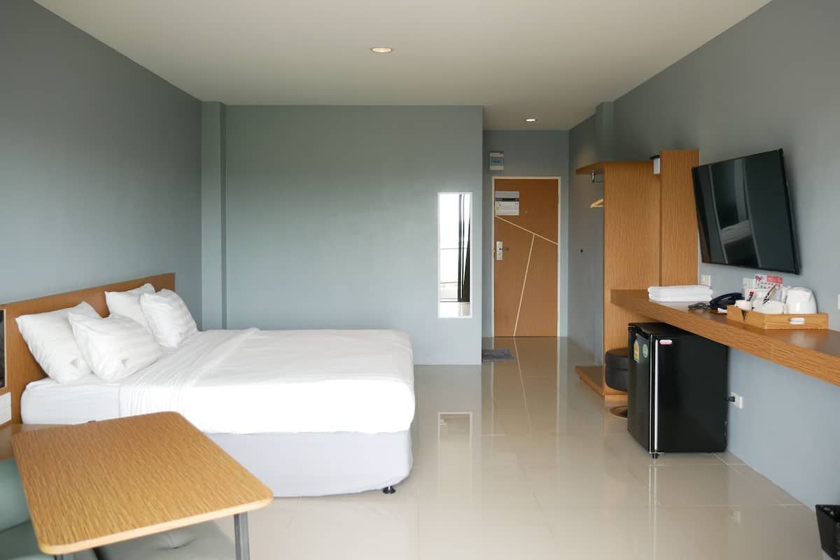 A modern hotel room with a bed, a desk, a TV, and a refrigerator.