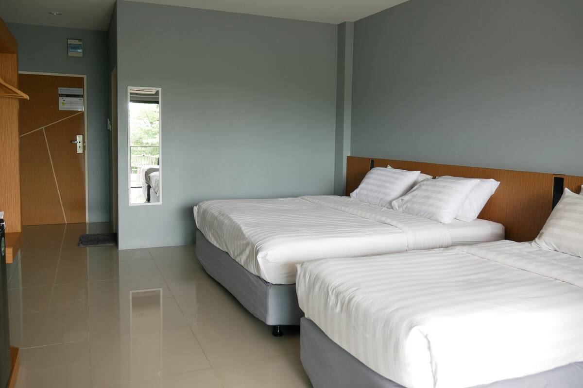 A hotel room with two beds, a wooden headboard, a small window, and a door leading to a balcony.
