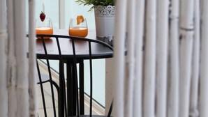 Ein Balkon mit Tisch und Stühlen, einem Blumentopf und zwei Getränken mit Früchte-Garnitur.