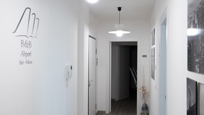 Ein Flur mit Holzboden, weißen Wänden und einer Deckenleuchte. Links befindet sich eine Tür und rechts ein gerahmtes Bild.