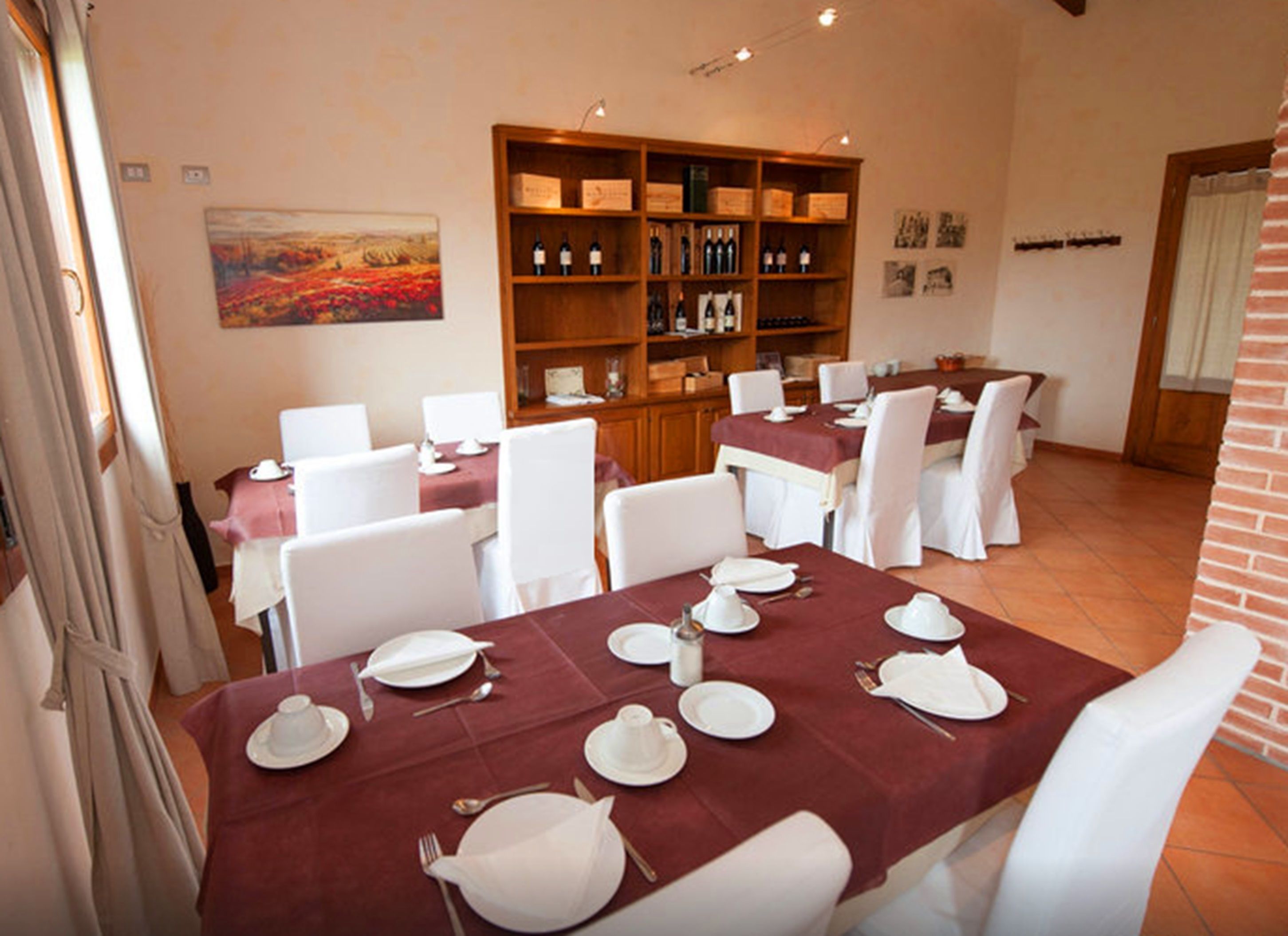A dining area with tables set for four, white chairs, a wooden wine rack, and a painting on the wall.