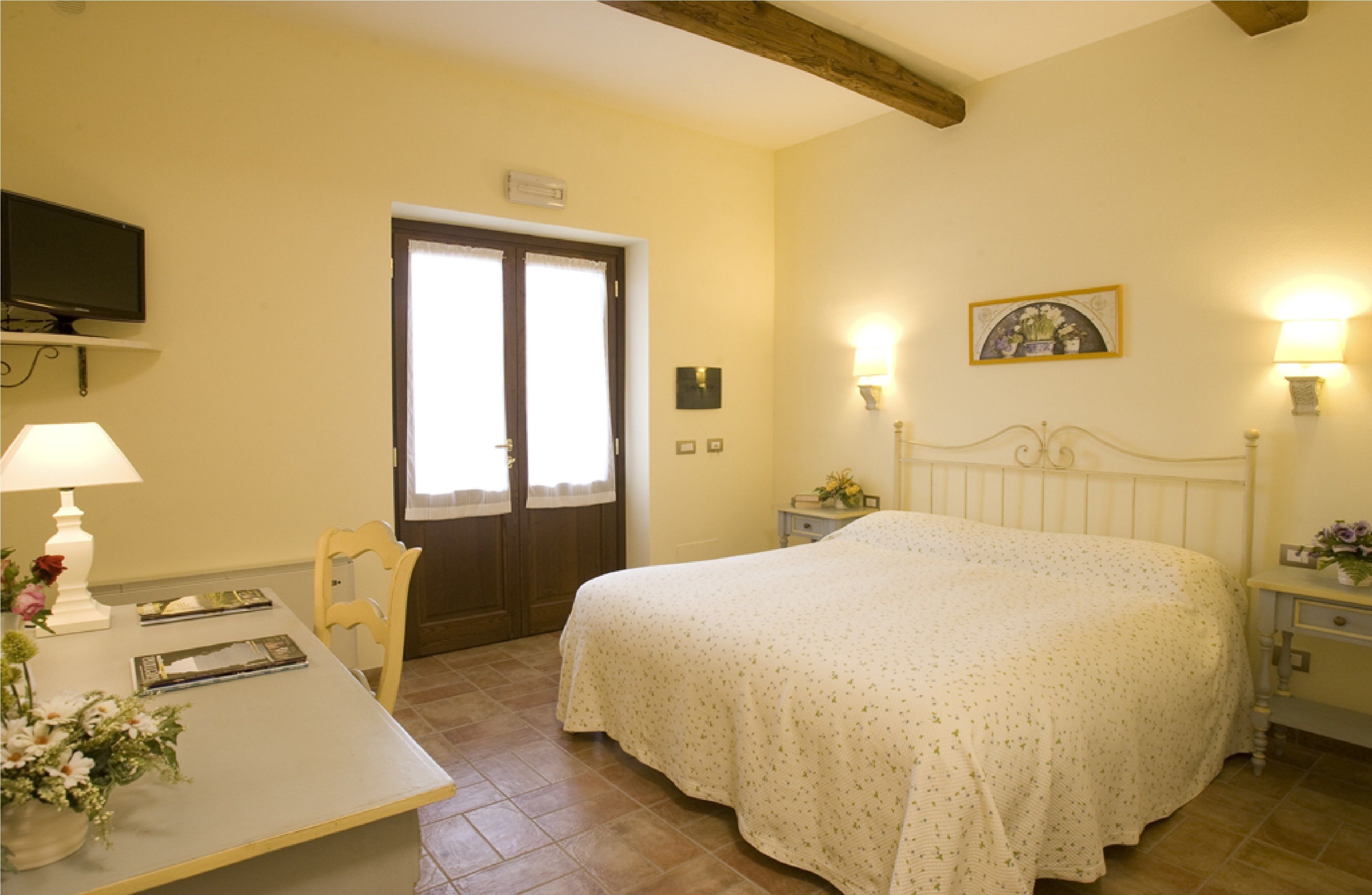 A bedroom with a bed, a desk, a chair, a television, and a door.
