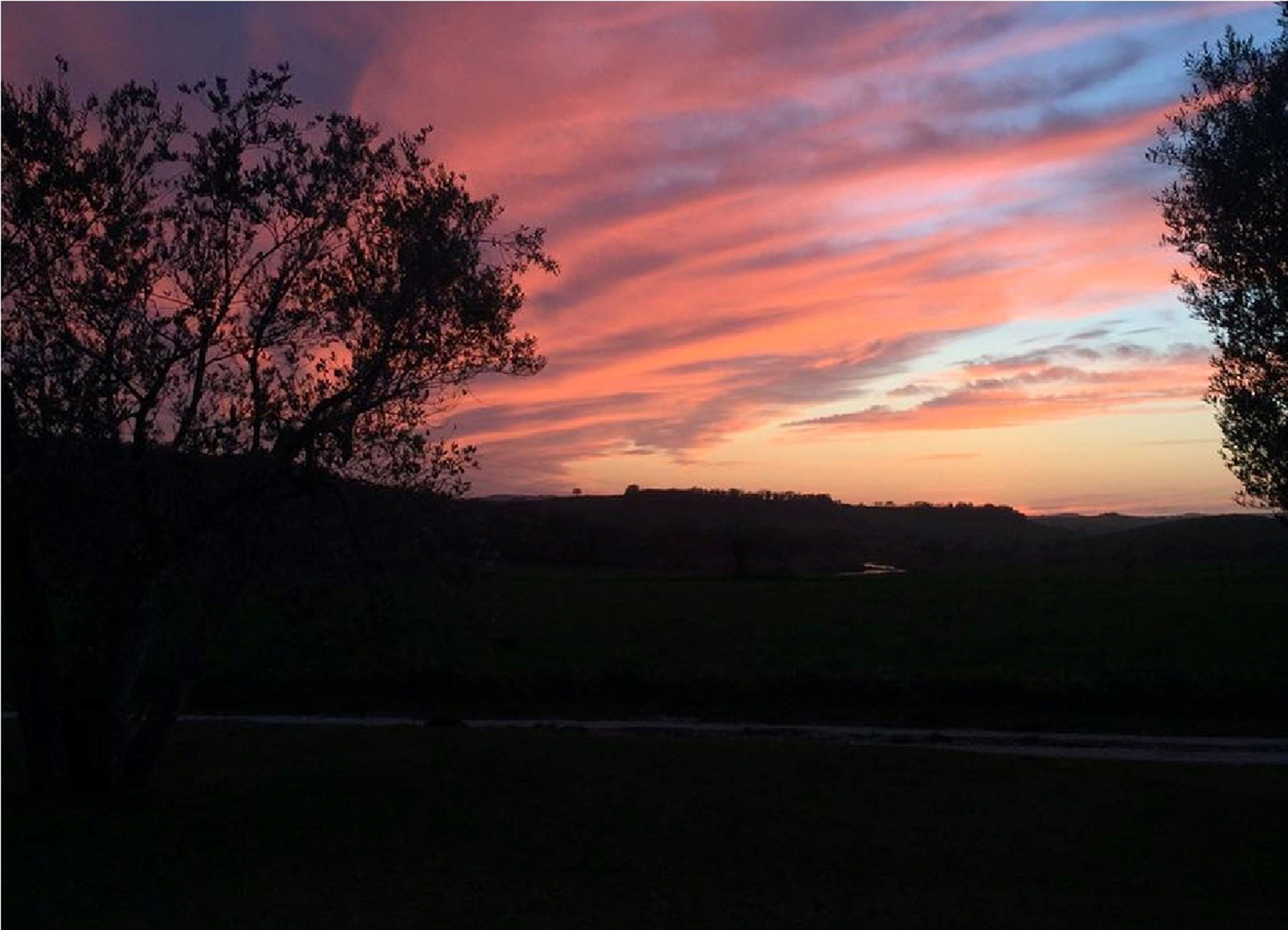 A sunset over a rural landscape with trees silhouetted against the sky.