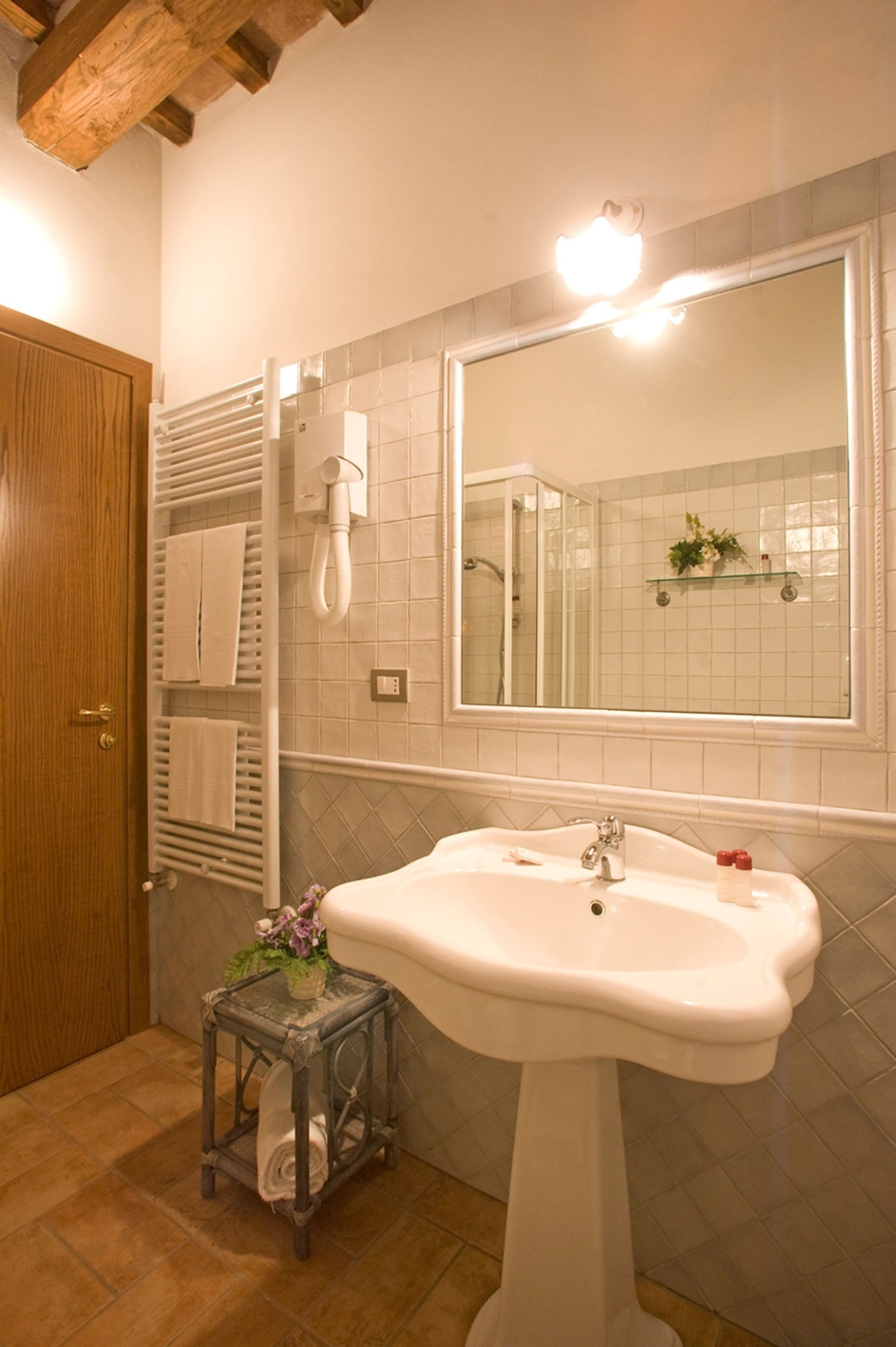 A bathroom with a pedestal sink, a mirror, a towel rack, and a small table with a vase.