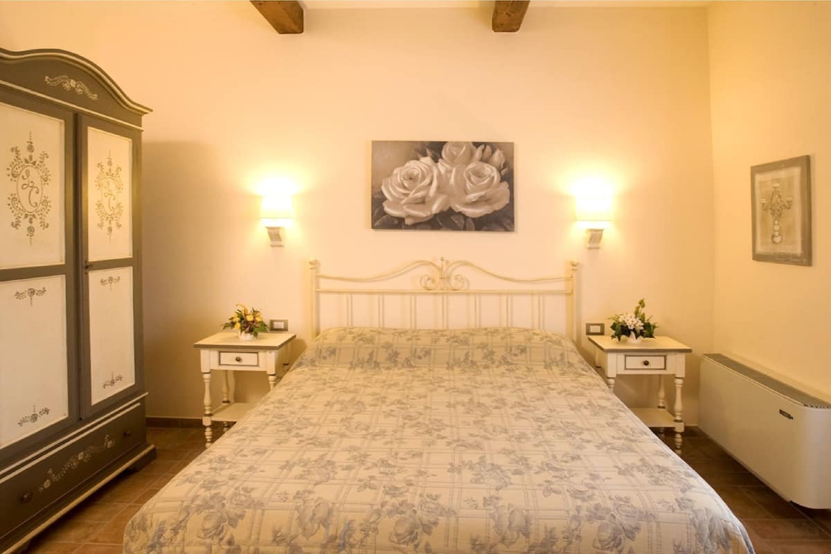 Une chambre à coucher avec un lit, deux tables de chevet, une armoire et un tableau représentant des roses accroché au mur.