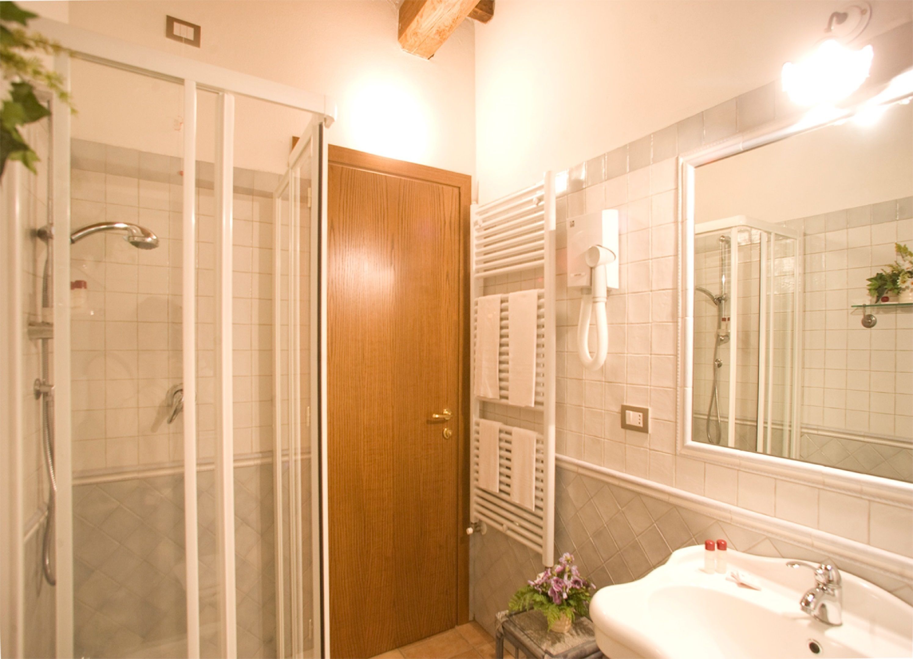 A bathroom with a glass shower enclosure, a wooden door, a white sink with a mirror, and a towel rack.