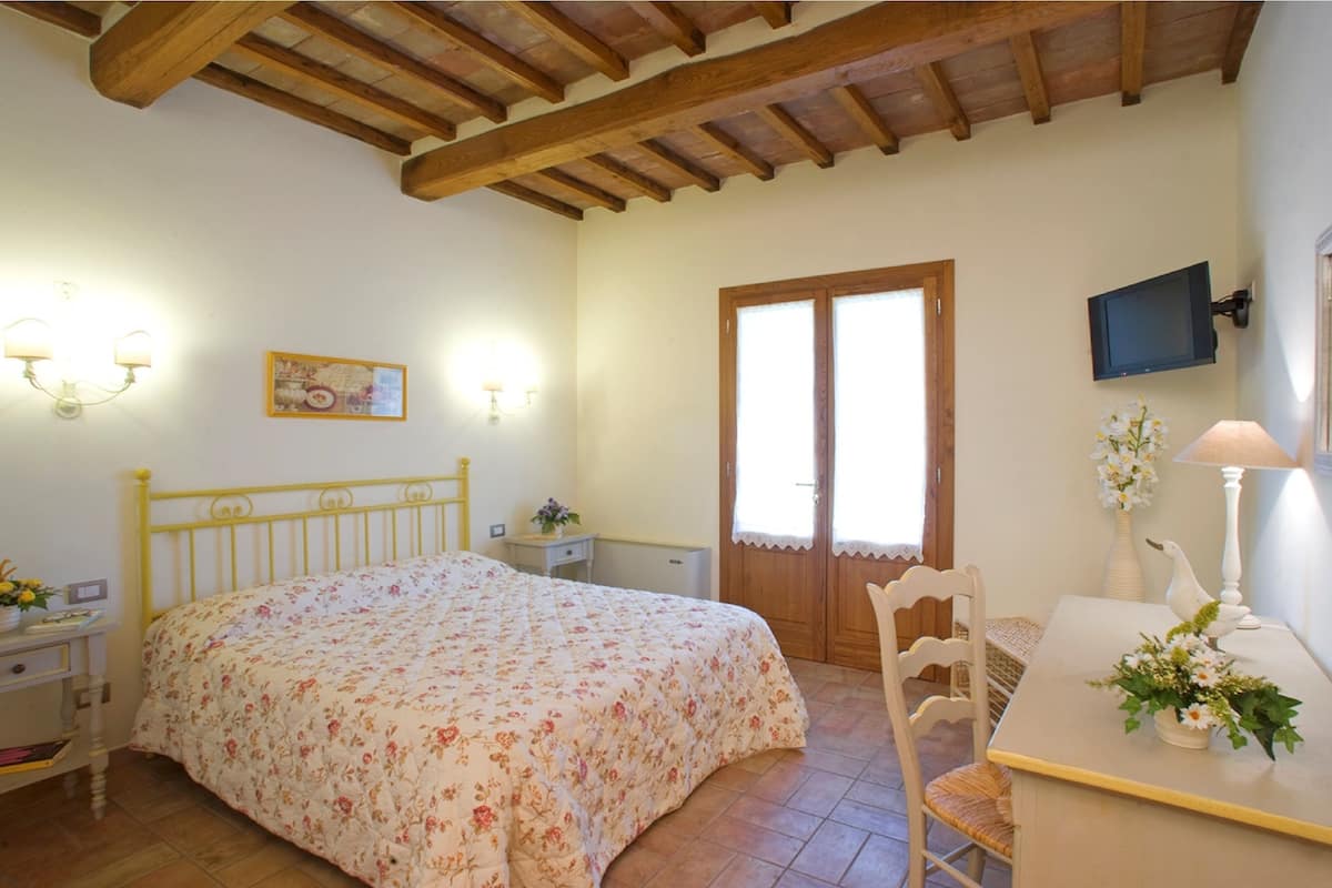 Une chambre à coucher comprenant un lit, une table de chevet, une lampe, une chaise et un téléviseur fixé au mur.