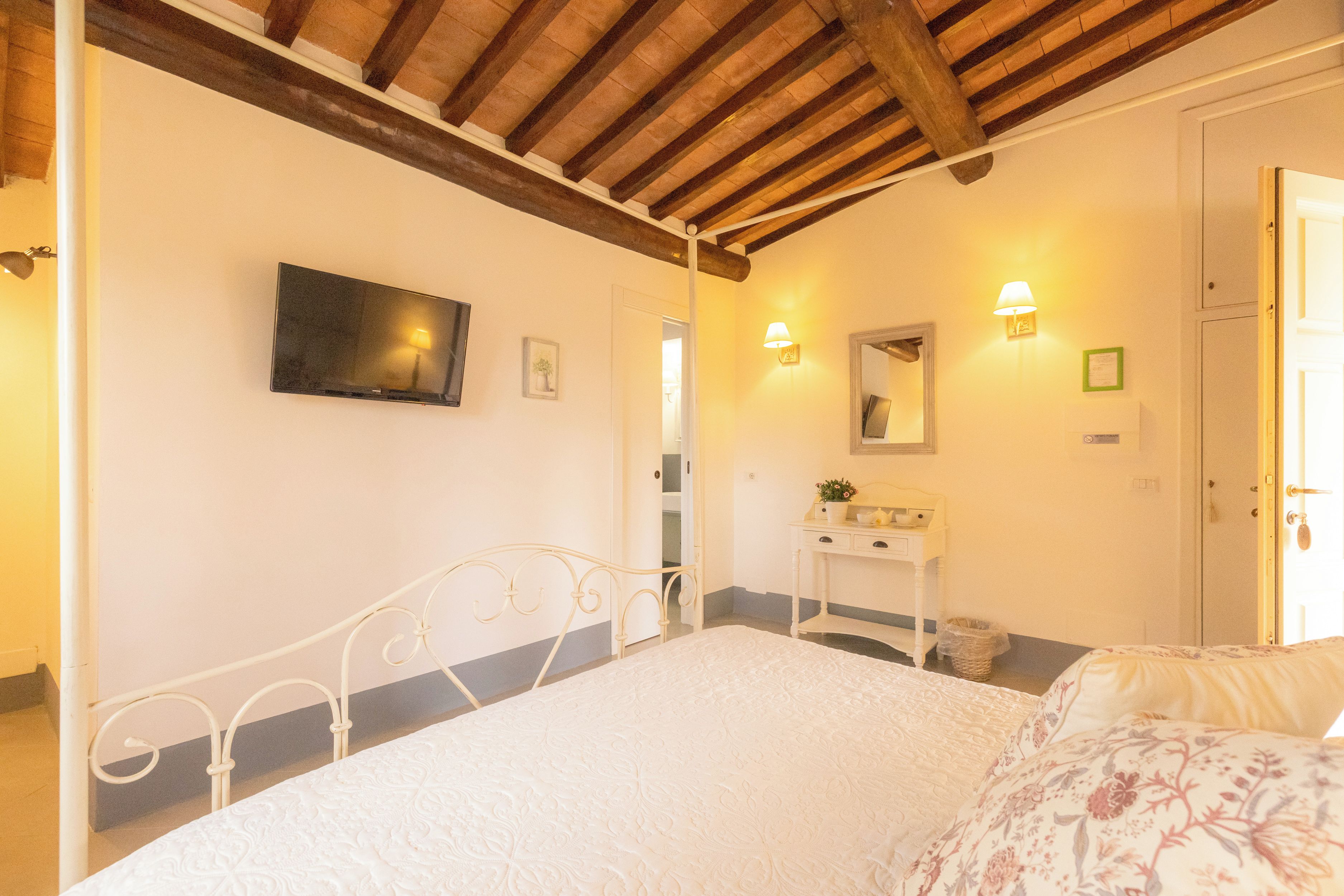 Ein Schlafzimmer mit einem Bett, einem Nachttisch, einem Spiegel und einem an der Wand befestigten Fernseher.