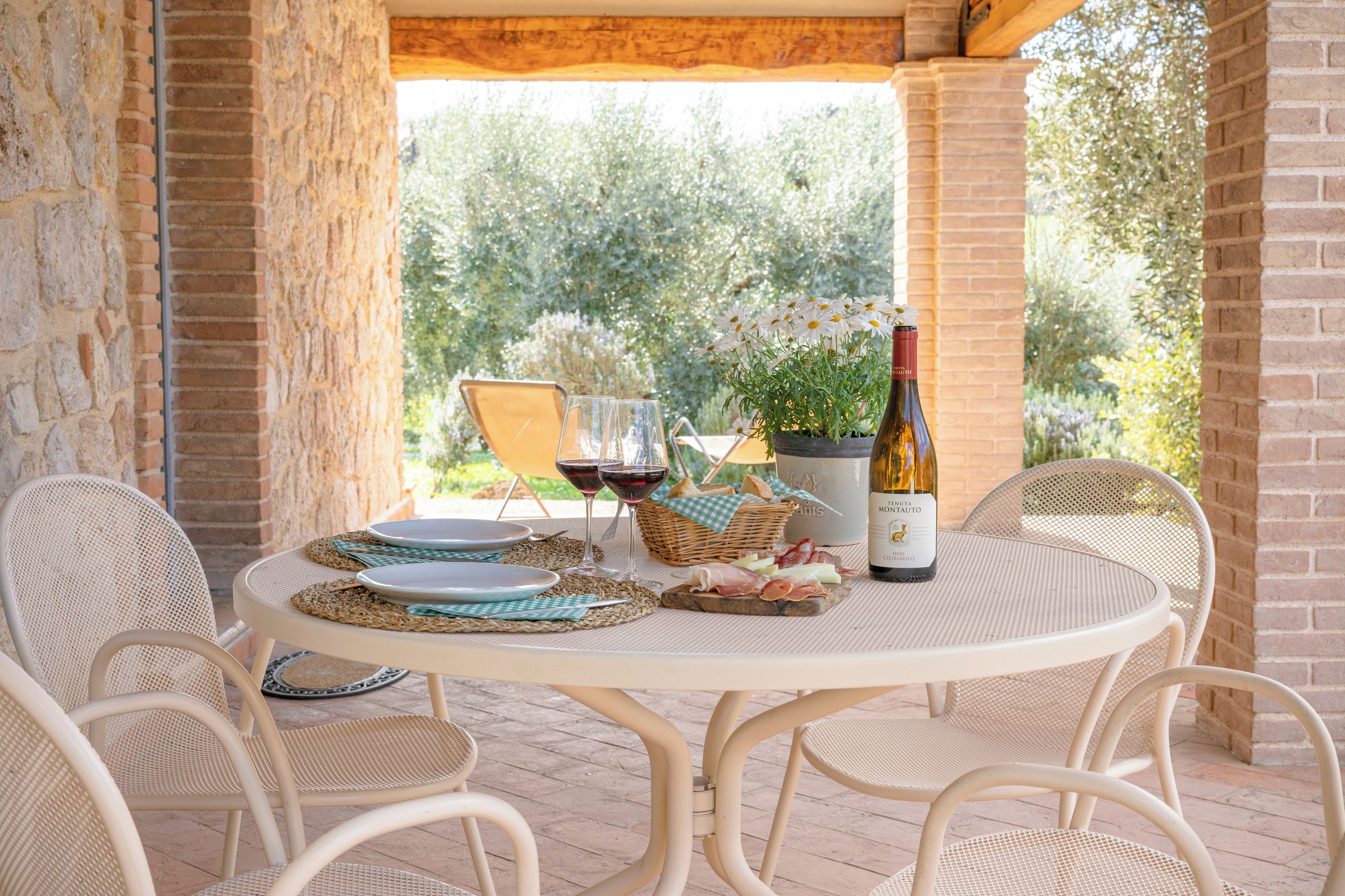Een terras buiten met een ronde eettafel, omringd door rieten stoelen.
