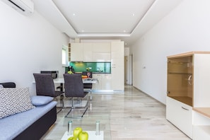 A modern living room with a sofa, chairs, a glass coffee table with apples, and a kitchen in the background. - Luxury Apartments Kostrena (Kostrena)