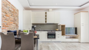 A modern kitchen with white cabinets, a brick wall, and a dining area with two chairs. - Luxury Apartments Kostrena (Kostrena)