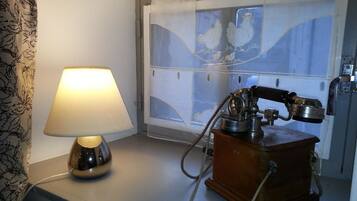 A room with a lamp, a vintage telephone, and a window with a view of chickens.