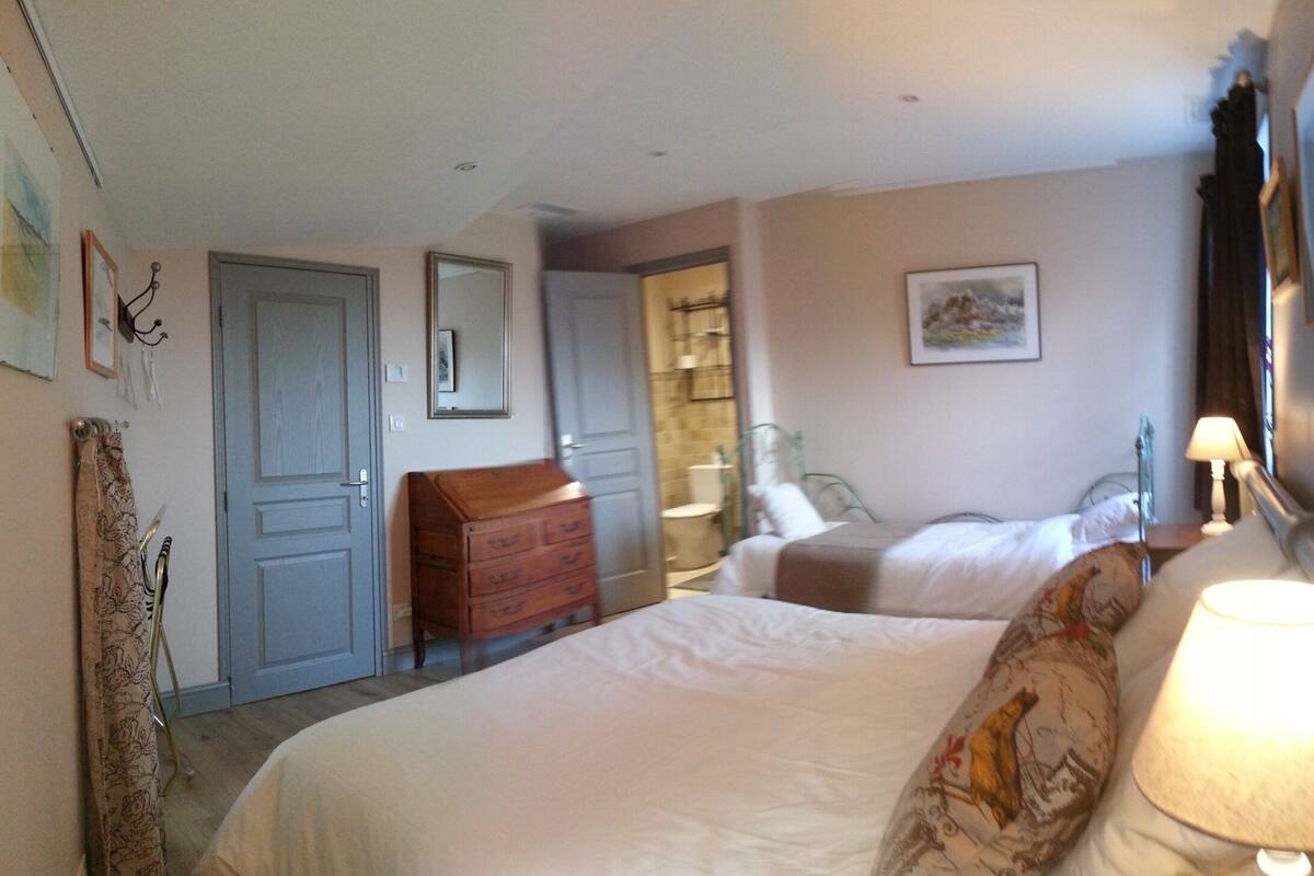 A hotel room with two beds, a wooden dresser, a mirror, and a door leading to a bathroom.