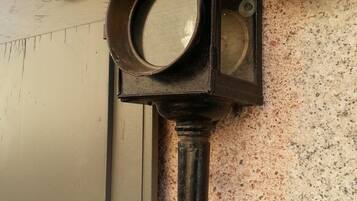 Une lanterne murale dotée d’un miroir rond et d’un interrupteur, fixée à un mur texturé près d’une porte.