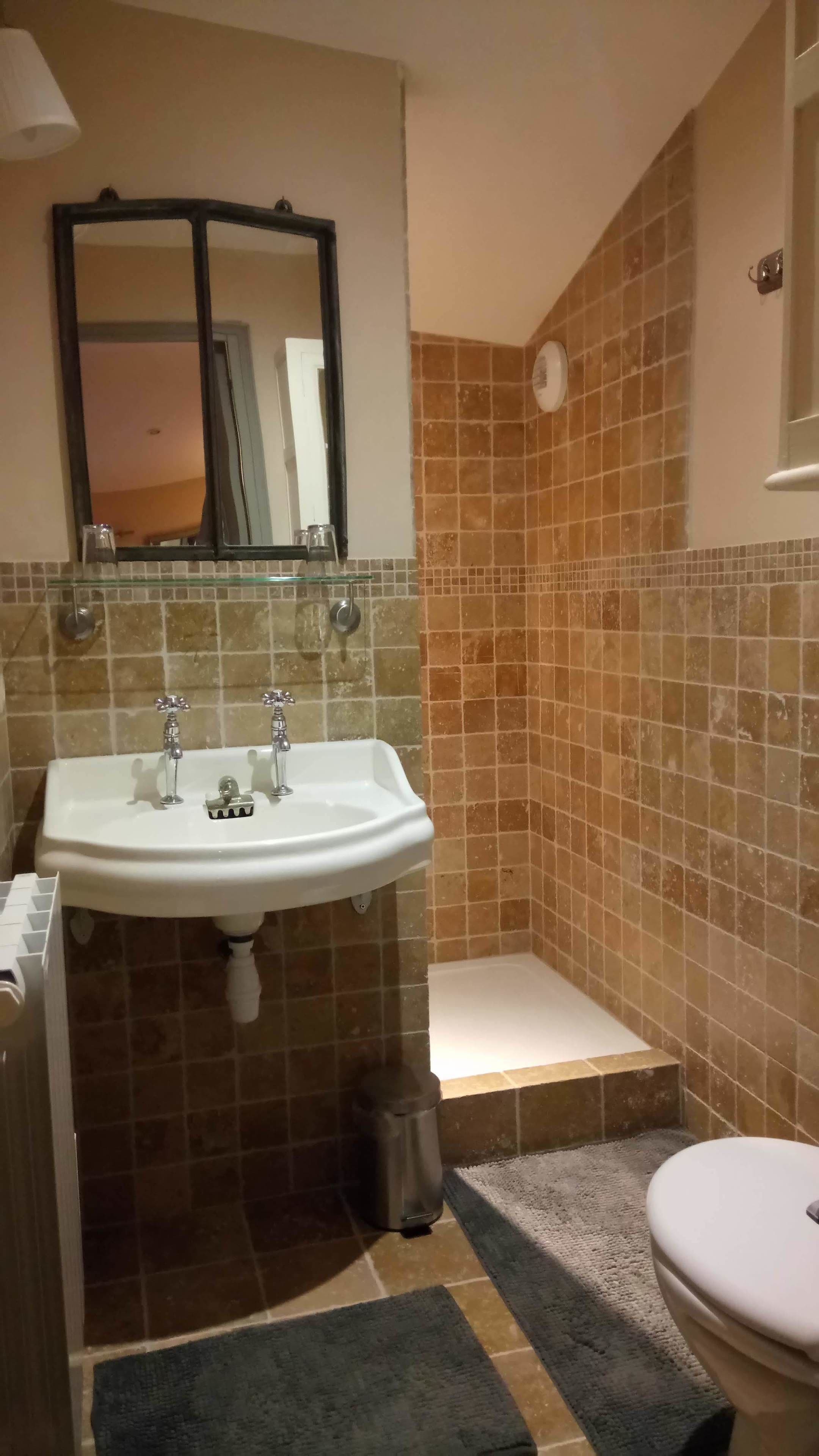 A bathroom with a white sink, two faucets, a mirror, a toilet, and a small step leading to a bathtub.