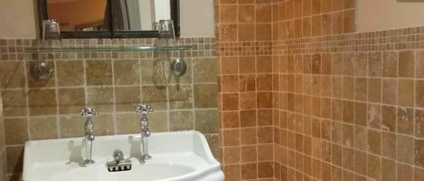 A bathroom with a white sink, two faucets, a mirror, a toilet, and a small step leading to a bathtub.