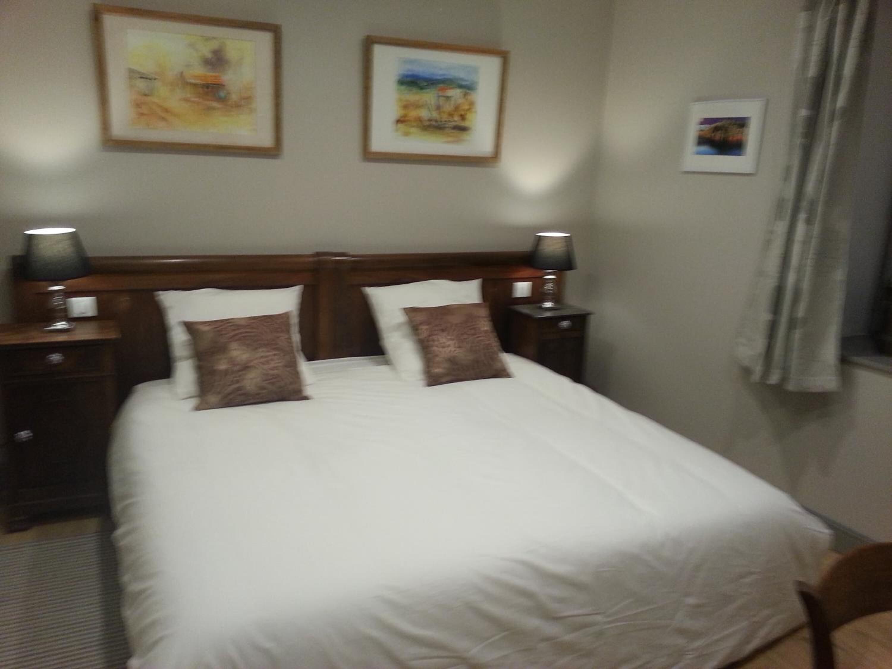 A neatly made bed with two pillows, a wooden headboard, and two bedside lamps.