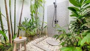 A shower area with a rain showerhead, surrounded by lush green plants and a pebble pathway. - Villa Maviba Seminyak (Seminyak)