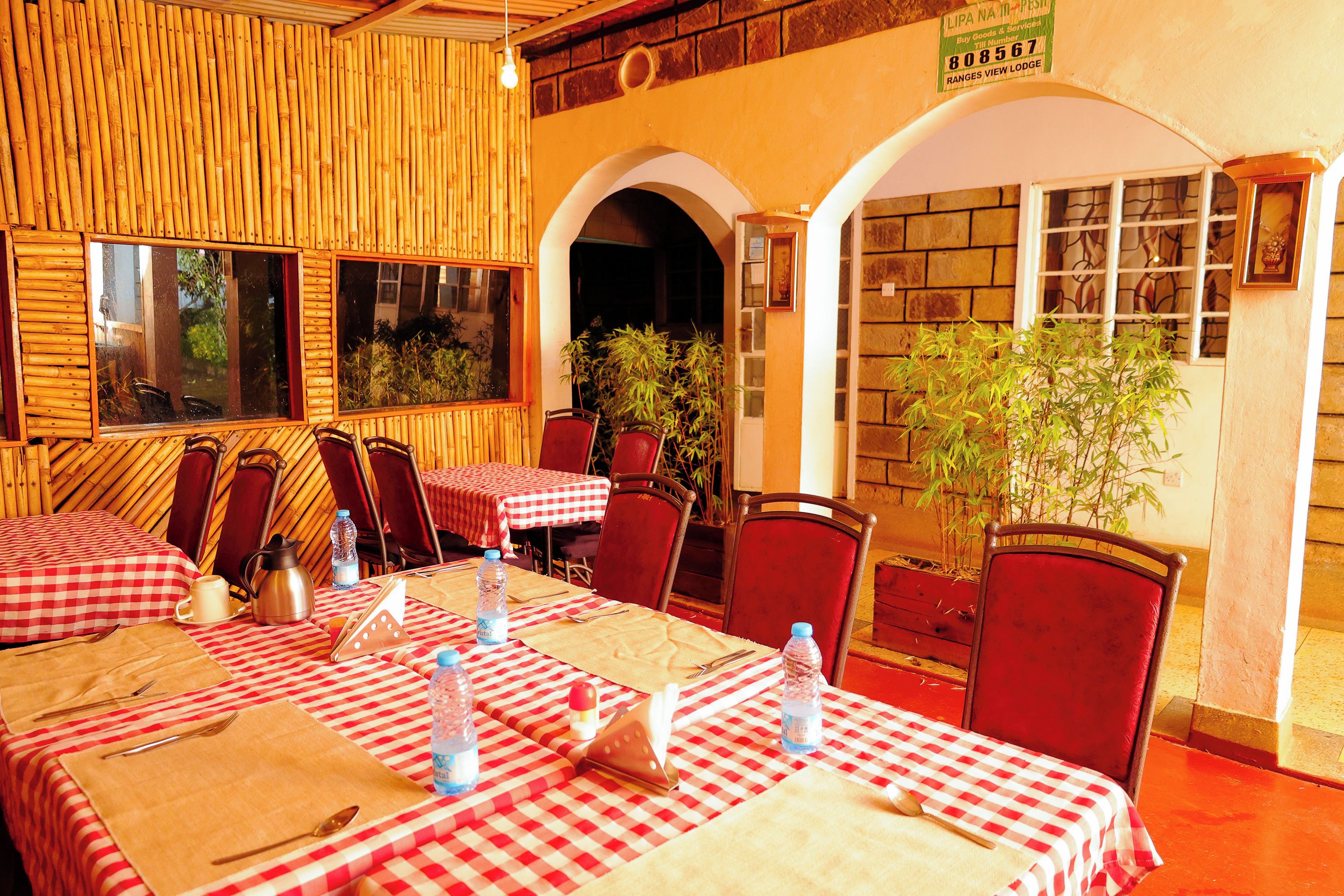 A restaurant with checkered tablecloths, red chairs, and a bamboo wall.