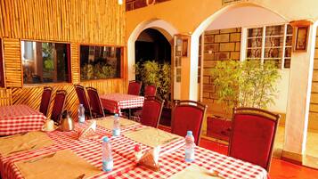 A restaurant with checkered tablecloths, red chairs, and a bamboo wall.