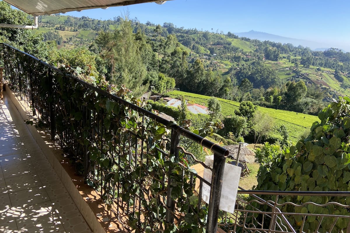 A balcony with a view of lush green hills and a distant mountain range.