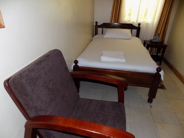 A neatly made bed with a wooden headboard, a wooden chair, and a small bedside table with a water bottle.