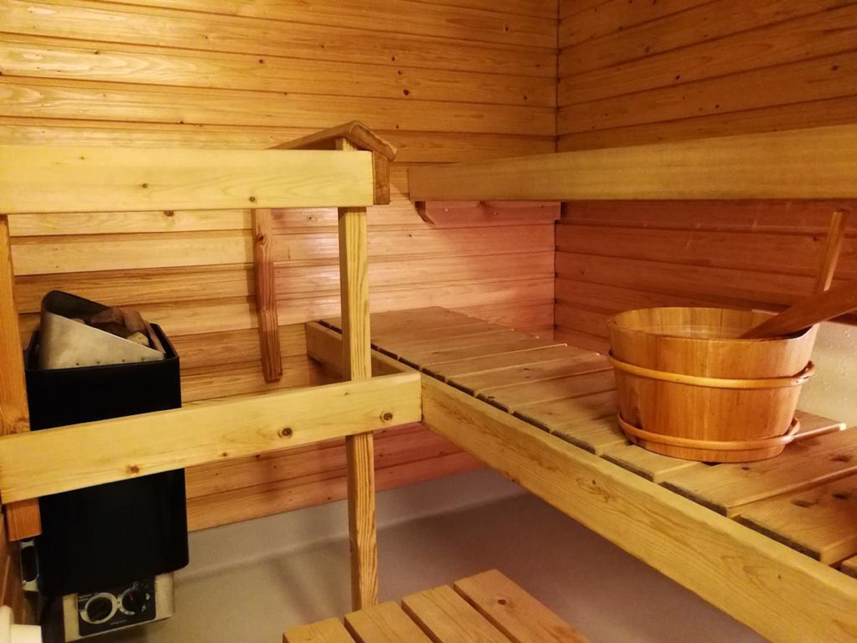 A wooden sauna room with benches, a wooden bucket, and a black heater.