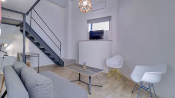 A modern living space with a grey sofa, a small table with a potted plant, a TV on a stand, and a staircase.
