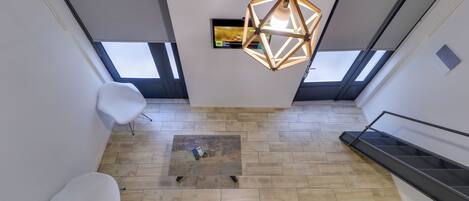 A modern interior with a wooden floor, a geometric pendant light, a flat-screen TV, and a staircase.