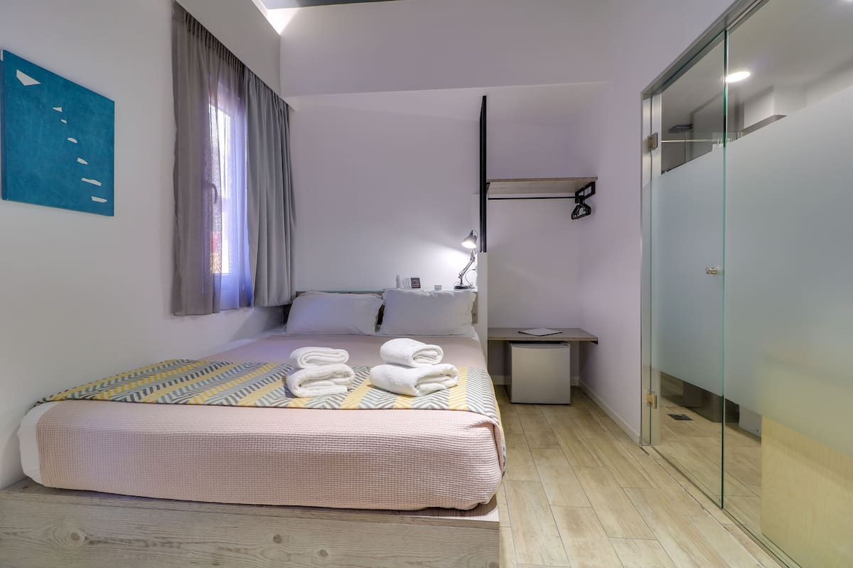 Quarto moderno com cama, mesa de cabeceira, abajur e divisória de vidro.