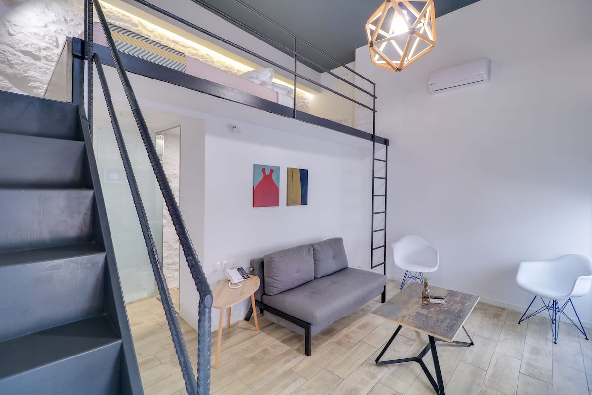 Um espaço moderno com escada, sofá, mesa e escabela.
