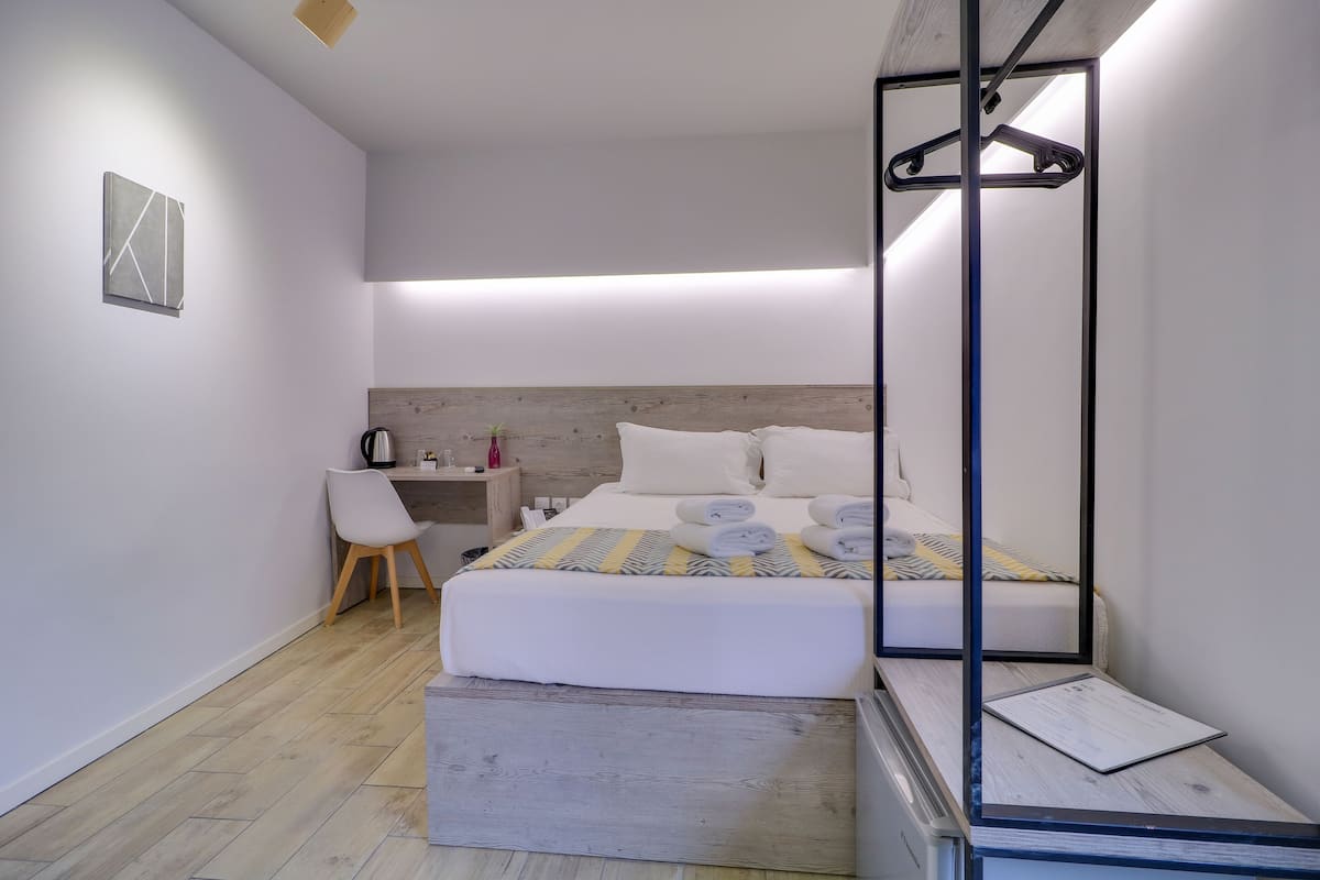 Quarto moderno com cama, mesa de cabeceira, cadeira e espelho com cabide.