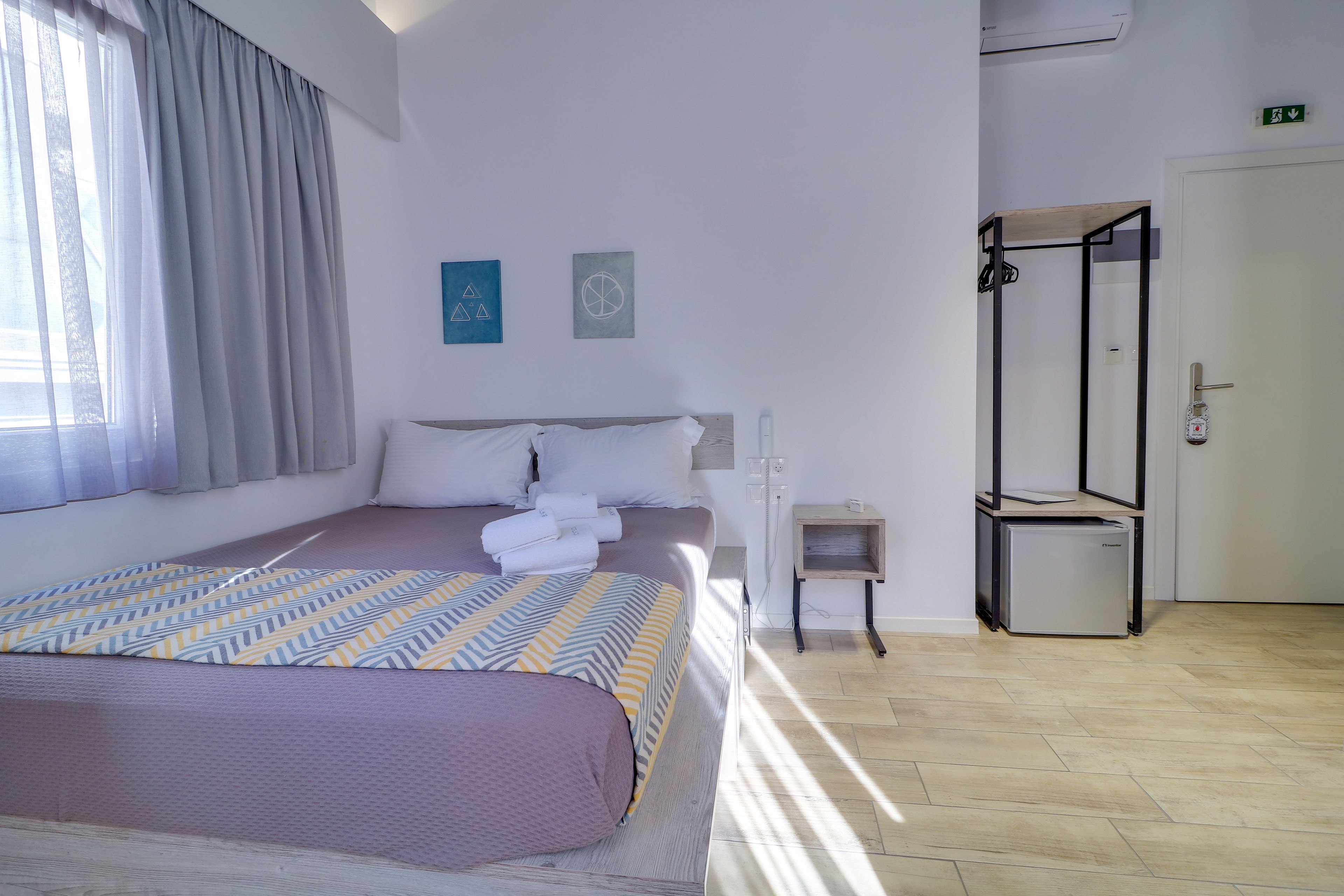 A hotel room with a bed, a small bedside table, a mirror, and a door.