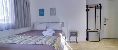 A hotel room with a bed, a small bedside table, a mirror, and a door.