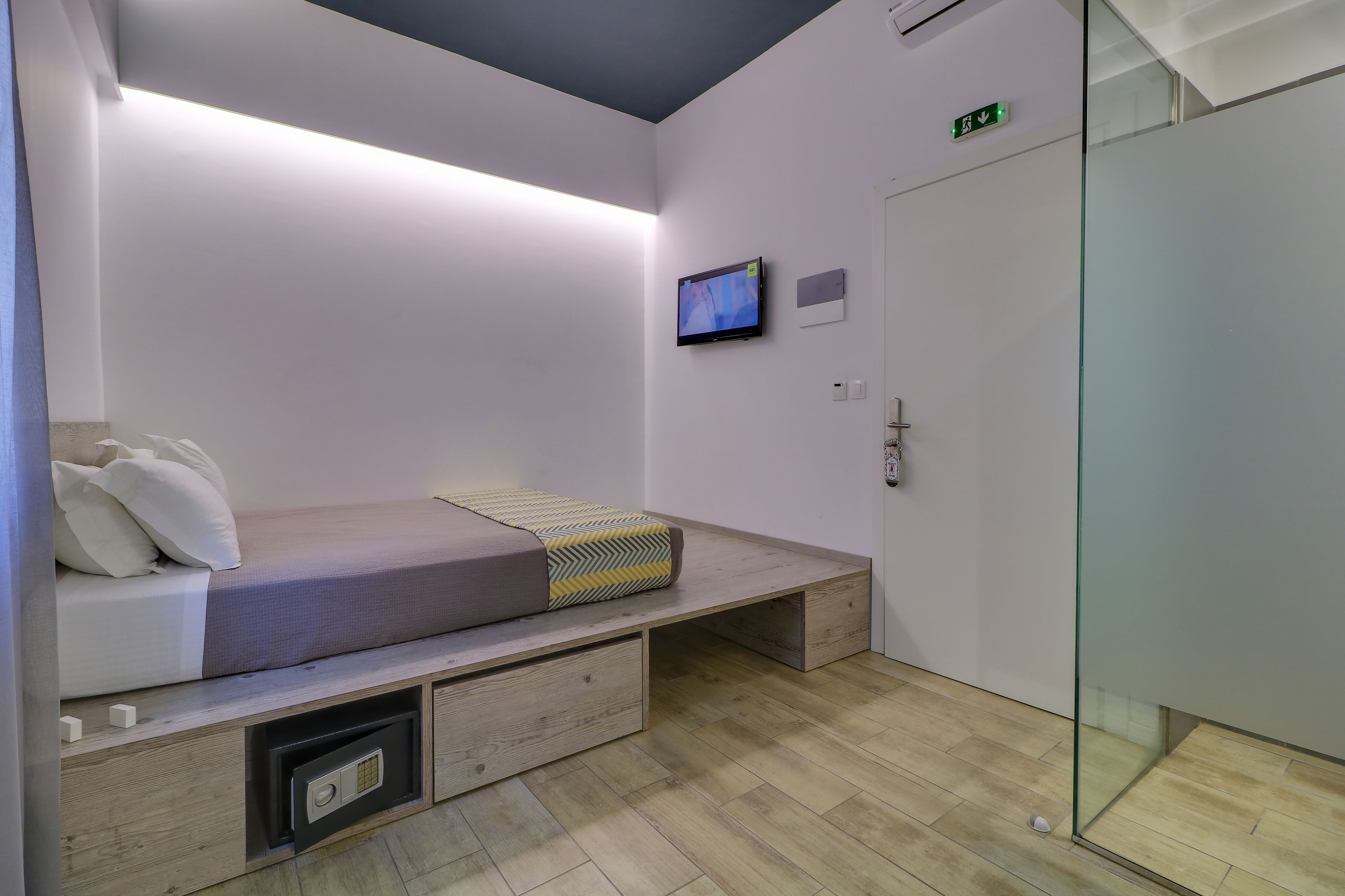 A modern bedroom with a bed, bedside storage, a TV, and a glass partition.
