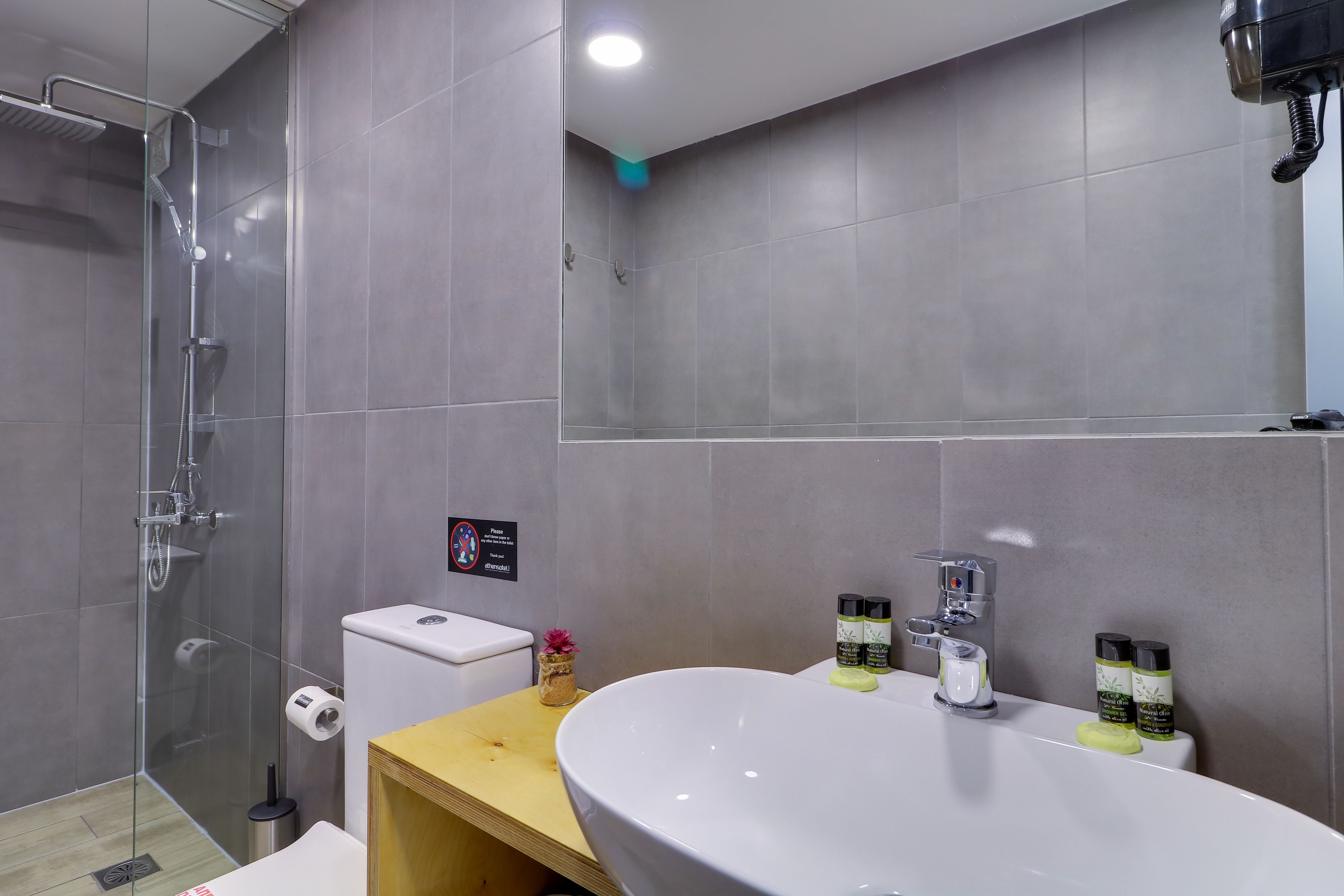 A modern bathroom with a glass-enclosed shower, a toilet, a sink with toiletries, and a mirror.