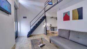 A modern living room with a grey sofa, a wooden coffee table with a remote control, a TV on the wall, and a staircase leading to another level. - athensotel (Athens)