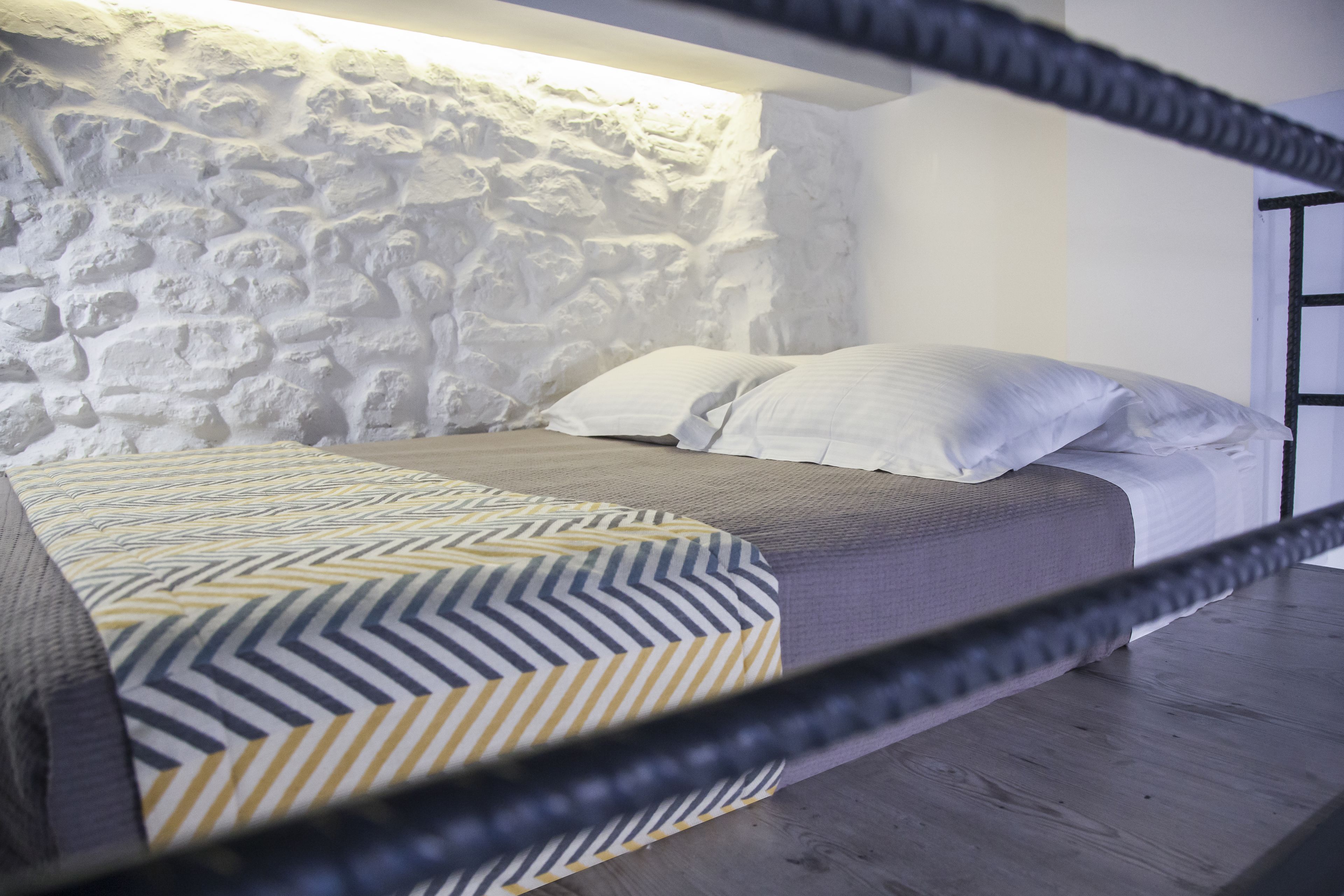 A bunk bed with a patterned bedspread, a stone wall, and a wooden floor.
