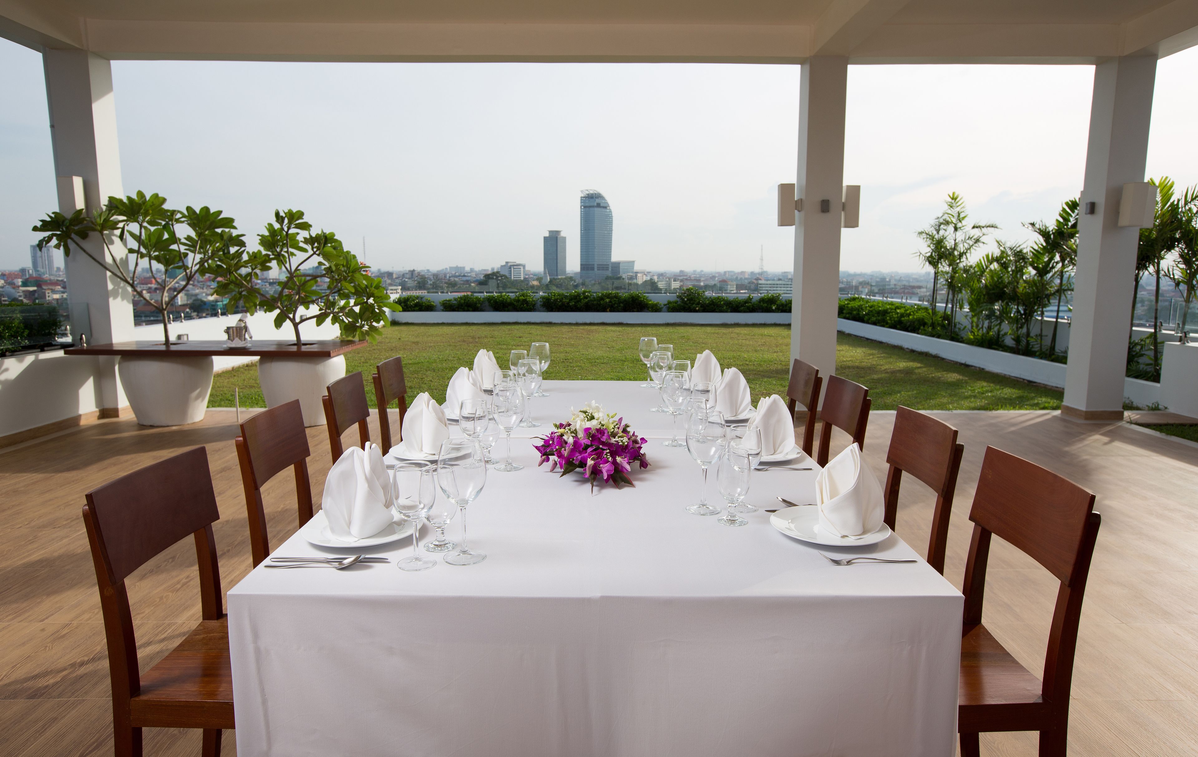 Mesa para ocho personas con vistas a la ciudad, mantel blanco y un centro de mesa con flores moradas.