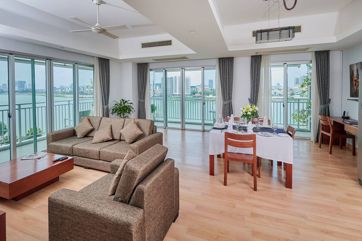 A modern living room with a sofa, a dining table set for two, and a kitchen area with a refrigerator.