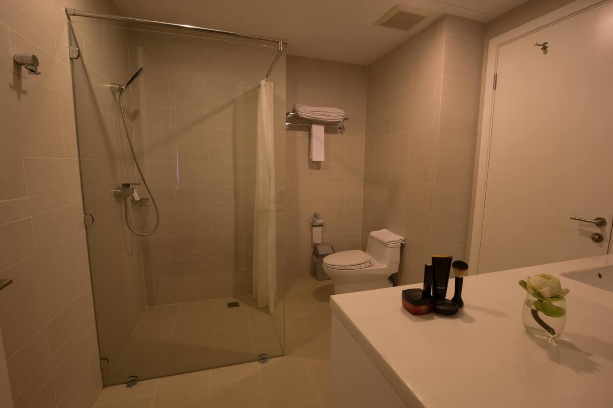A modern bathroom with a glass shower enclosure, a white toilet, and a bathtub with toiletries on the counter.