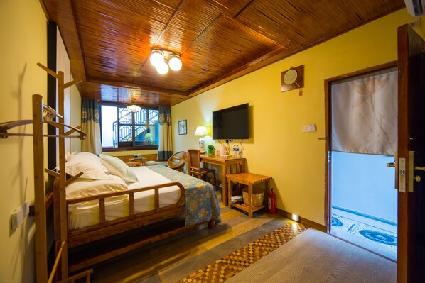 Quarto com cama de madeira, escrivaninha com luminária, televisão e vista para o exterior.