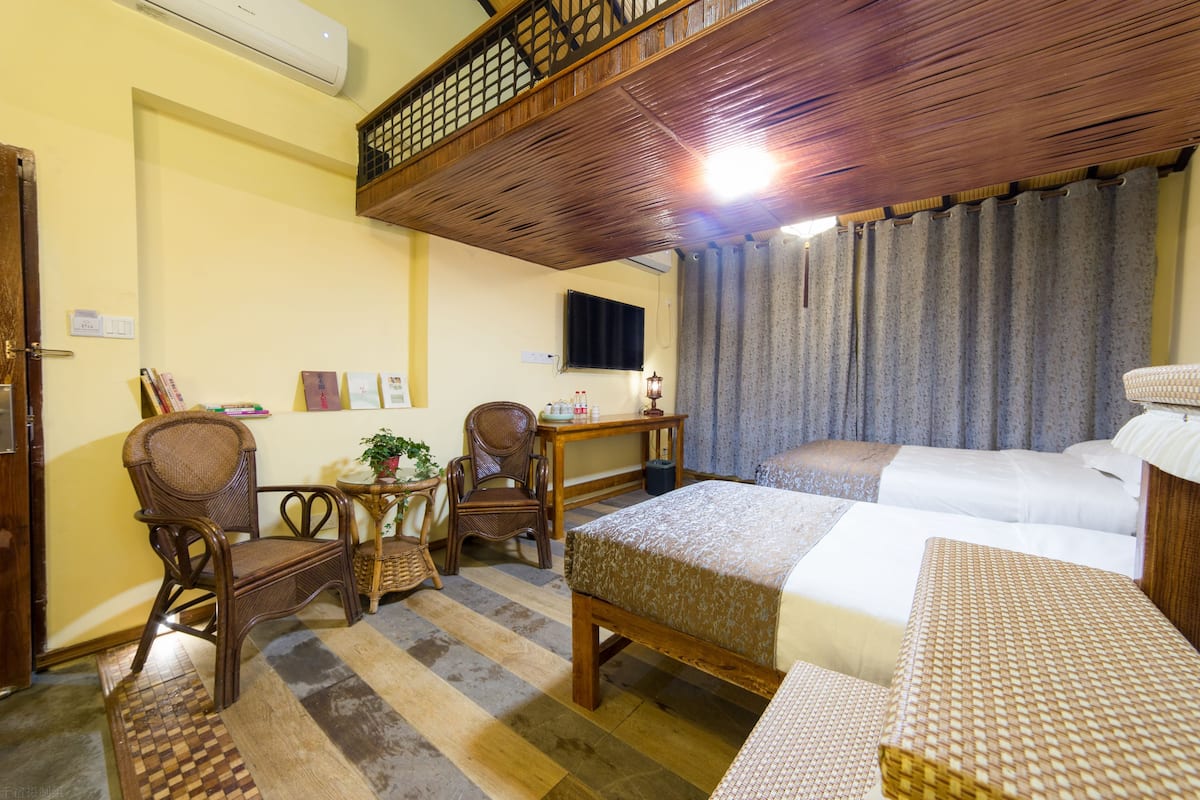 Habitación de hotel con techo de madera, dos camas, una mesita pequeña, dos sillas y un televisor.