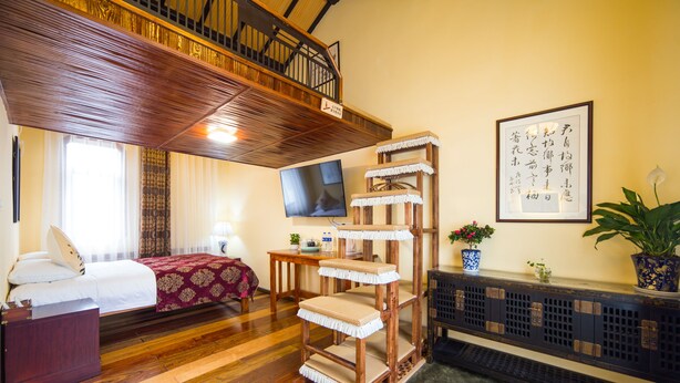 A hotel room with a wooden floor, a bed with a red and white bedspread, a wooden cat tree, a television, and a framed calligraphy piece on the wall. - Hemu Shantang Street (Suzhou)