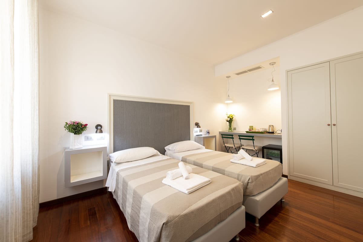 A hotel room with two beds, a desk, a wardrobe, and a small bathroom area.