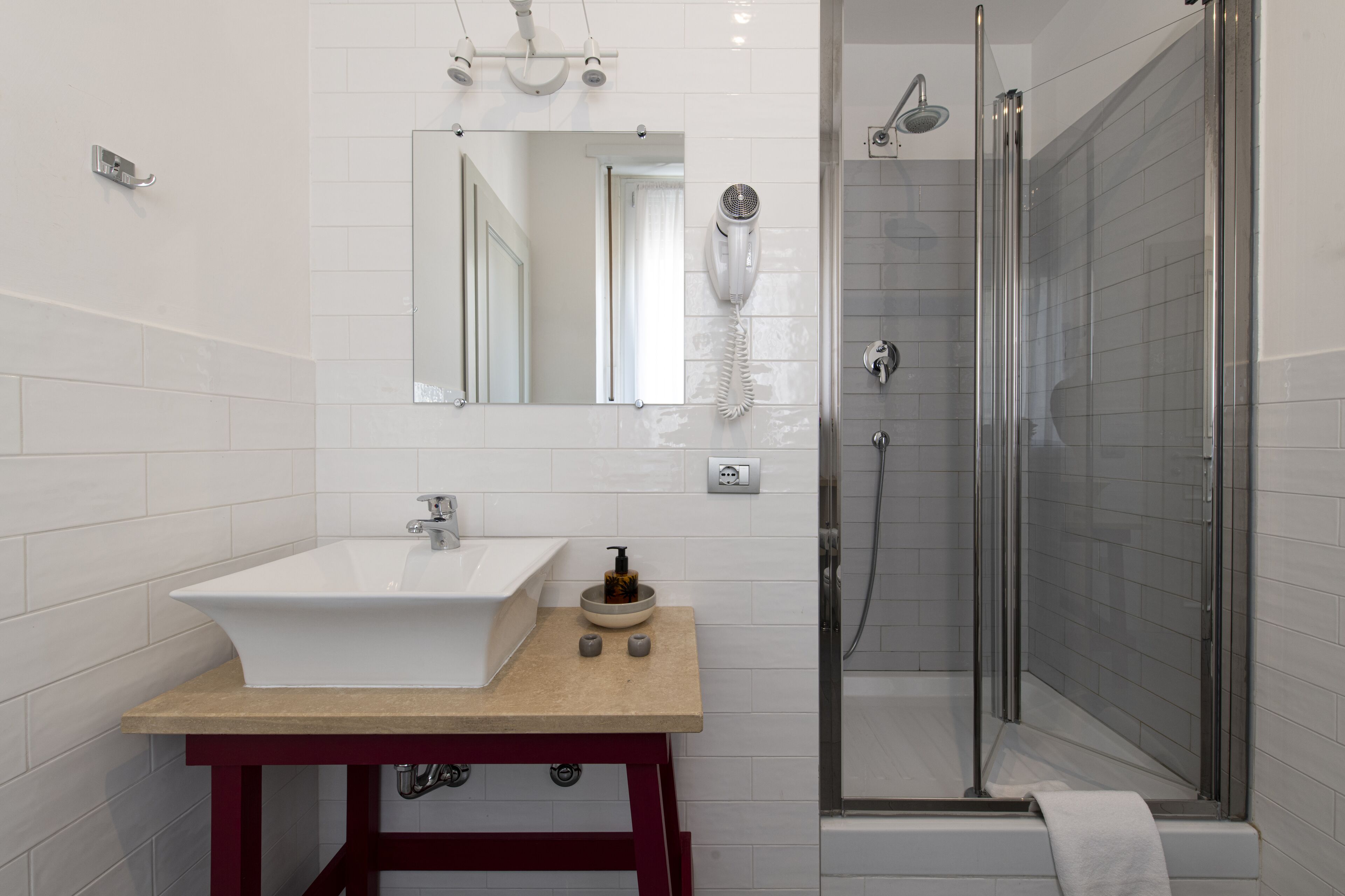 A modern bathroom with a white sink, a mirror, a handheld hair dryer, and a glass-enclosed shower.